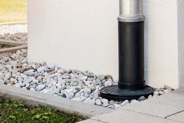 Downspout or Downpipe into French Drain Stones Floor Around Wall Building Outside. Modern Drainage System for Stormwater or Rainwater with Gravel Stones Covering by House Wall. - obrazy, fototapety, plakaty