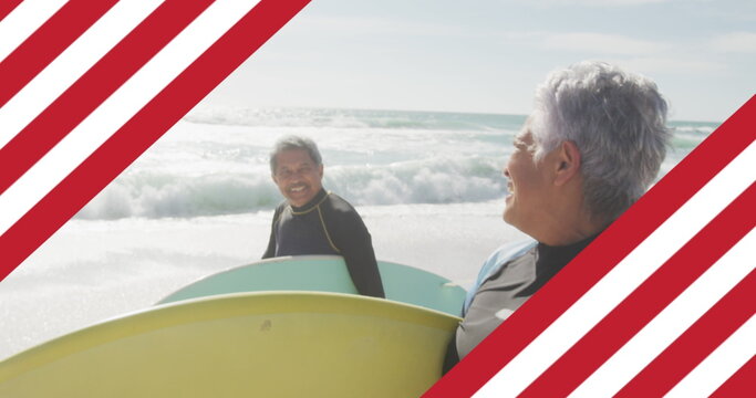 Image of flag of united states of america over senior biracial couple with surfboard on beach