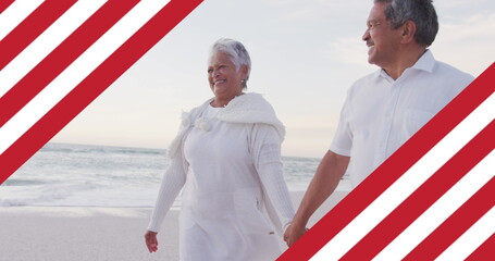 Image of flag of united states of america over senior biracial couple holding hands on beach