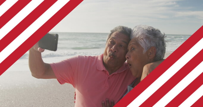 Image of flag of united states of america over senior biracial couple taking selfie on beach