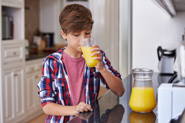 Children, kitchen and boy drinking orange juice from glass in morning for diet, health or...
