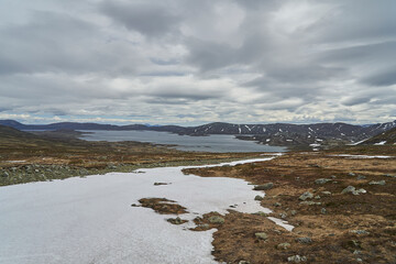 lake in the mountainous landscape of Jotunheimen in Norway, with snow covered peaks in the background, a popular travel destination for hiking.