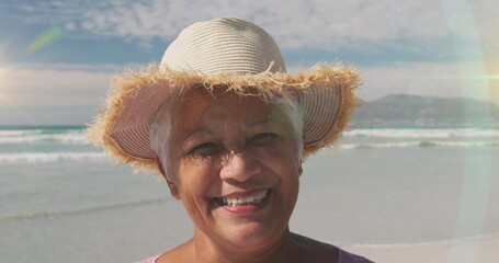 Image of glowing light over senior woman smiling by seaside