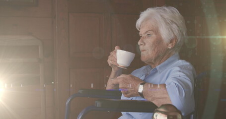 Image of glowing light over serious senior woman drinking tea