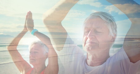Image of glowing light over senior couple practicing yoga by seaside