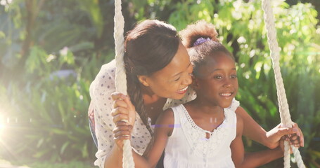 Spot of light against african american pushing her daughter on the swing in the garden