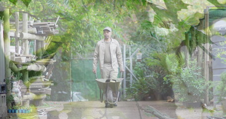 Composite image of tall trees against asian senior man moving a garden cart in the garden