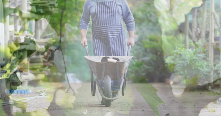 Composite image of hanging leaves against caucasian senior man moving a garden cart in the garden