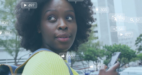 Image of social media notifications over happy african american woman using smartphone in street