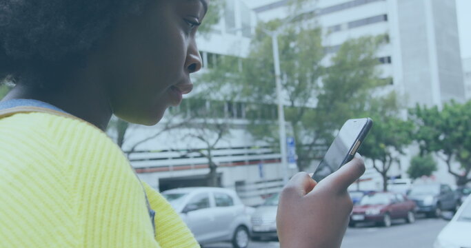 Image of social media notifications over happy african american woman using smartphone in street