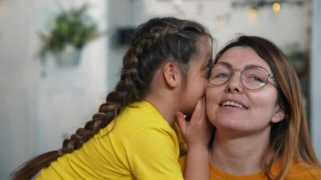 Happy family concept.baby whispers in mom's ear. child shares a secret. close-up portrait, daughter whispering secrets in her mother's ear. close relationship between child and mother. trust in family