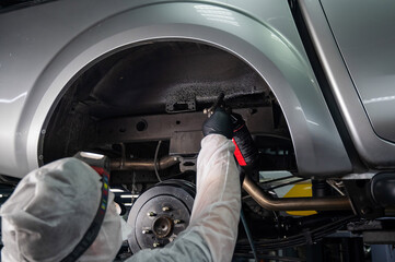 An auto mechanic applies anti-corrosion mastic to the underbody of a car.