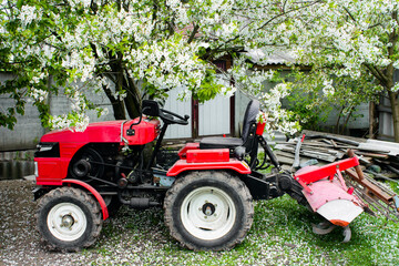 Red small modern mini tractor standing at the farm against the background of a spring landscape....