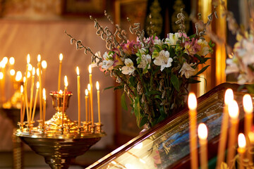 Palm Sunday. candles burn in an Orthodox church in front of the icon, against the background of willow and flowers