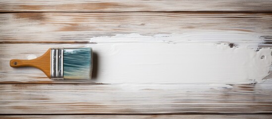 A paint brush rests on a hardwood table in a rectangular shape. The room has wooden flooring and a large window with glass panes, casting tints and shades throughout the house