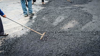 Damaged asphalt roads are being repaired by worker. Worker spreading asphalt on a road.
