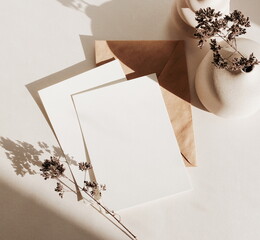 Greeting Cards mockup, empty white blanks, envelope dry flower in a vase, sunlight shadow top view on beige background with copy space. flat lay. Empty white Blank, card template, invitation.
