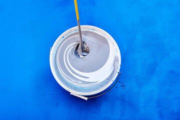 Stirring rod mixing and tinting paint for walls, house painter tinted paint in bucket on blue...