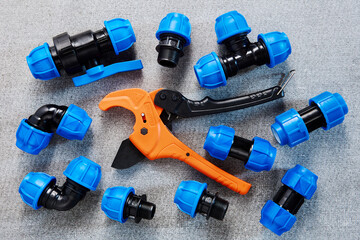 Ratchet plastic pipe cutter with adaptor fitting and compression clamp coupling lies on gray surface.