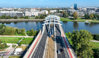 Krakow, Poland. Two blue trams passing each other on Kotlarski suspension bridge with four lane road, tramway, footbridge and red bicycle lane over Vistula river. Aerial view - 757812453
