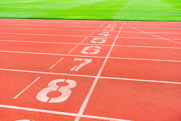 Red running track with green grass in stadium. Athletic competitions starting line positions from one to nine.