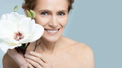 Middle-aged woman showcasing elegance with white magnolia flower on blue backdrop