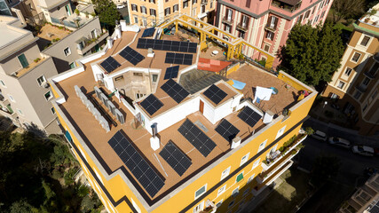 Aerial view of solar panels installed above the roof of an apartment building in a city. Green energy powers the condominium. © Stefano Tammaro
