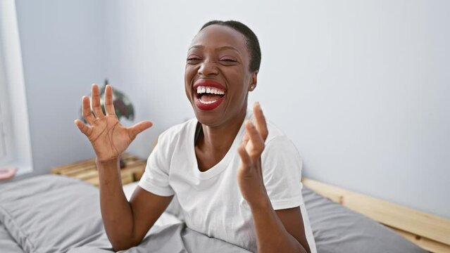 Excited african american woman celebrating madly in bedroom, joyful success win lying on bed, arms raised