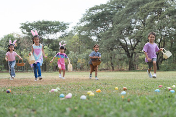 Happy group of diverse cute little children hunting Easter eggs, wearing bunny ears. kids holding...