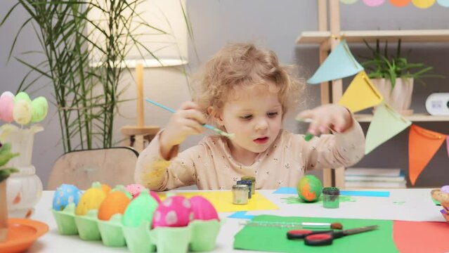 Vibrant egg dyeing activity. Painted eggs adding to the Easter celebration. Little toddler girl painting easter eggs in festive home interior funny infant kid enjoying decorating process