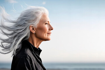 Beautiful mature woman with silver gray hair on a neutral sky background in profile position and the wind blowing, portrait