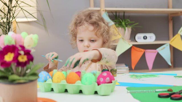 Easter egg painting tradition. Easter event for children. Painting Easter eggs with kids. Little toddler girl painting easter eggs in festive home interior