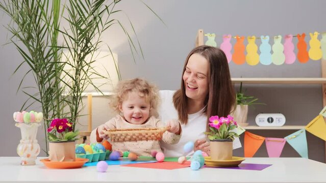 Satisfied cheerful delighted young woman with little daughter organizing Easter egg hunts for family and friends to enjoy in festive home interior enjoying traditional egg dyeing
