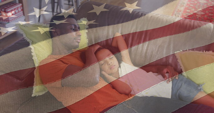 Naklejki Image of flag of usa waving over african american father lying on sofa with sleeping daughter