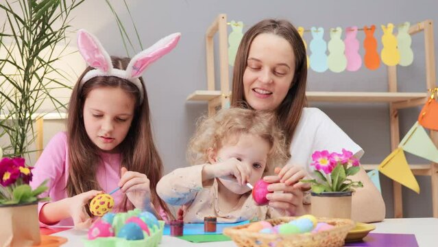 Optimistic woman with little daughters painting Easter egg in festive home interior family enjoying festive time together mother with children has funny preparation for holiday
