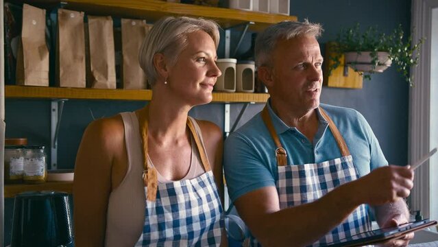 Mature Couple Working In Sustainable Plastic Free Grocery Store Checking Stock With Digital Tablet