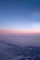 Orange sunset sky on a cloudscape seen from an airplane window over a snowy landscape 