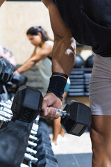 Fototapeta na wymiar Closeup shot of muscular male arm picking up heavy weights from dumbbell rack in modern gym