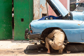 Cuban mechanic working on his car in the street, he is fixing an engine problem. Located in Havana city - Cuba