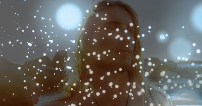 Glowing spots of light against caucasian man walking on the rocks near the sea