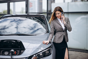 Business woman charging electric car and using mobile phone