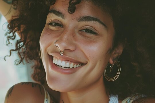A woman with a nose ring and earrings is smiling. She has a tattoo on her arm