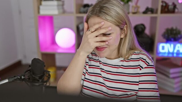 Blonde bombshell streamer caught giving the shock-peek! young damsel hides her flush-face behind her fingers in the dark gaming room.