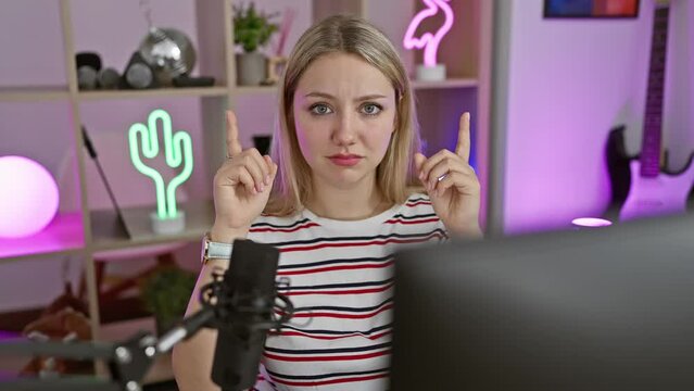 Depressed young woman streamer pointing upward in a dark gaming room, her blonde hair frames a sad, unhappy face glued to the computer