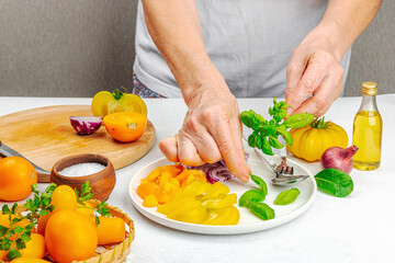 A woman is preparing a tomato salad. Ripe vegetables, herbs, aromatic spices, olive oil