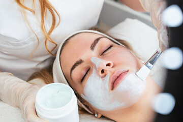 Obraz na płótnie Canvas Beautiful and attractive young adult woman receiving professional beauty or skincare treatment with herbal clay mask. Modern and popular facial care treatment concept. Spa salon. High angle view.