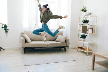 Joyful woman jumping on a sofa in a cheerful living room, expressing happiness and carefree...