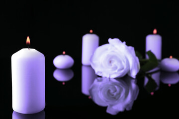 Fototapeta na wymiar Violet rose and burning candles on black mirror surface. Funeral attributes