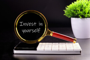 invest in yourself word through a magnifying glass on a black background with green grass in the background