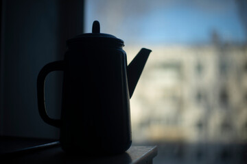 Kettle on background of window. Kettle with handle. Silhouette of kitchen utensils.